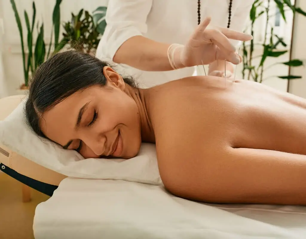 a woman lying down on a bed with acupuncture needles